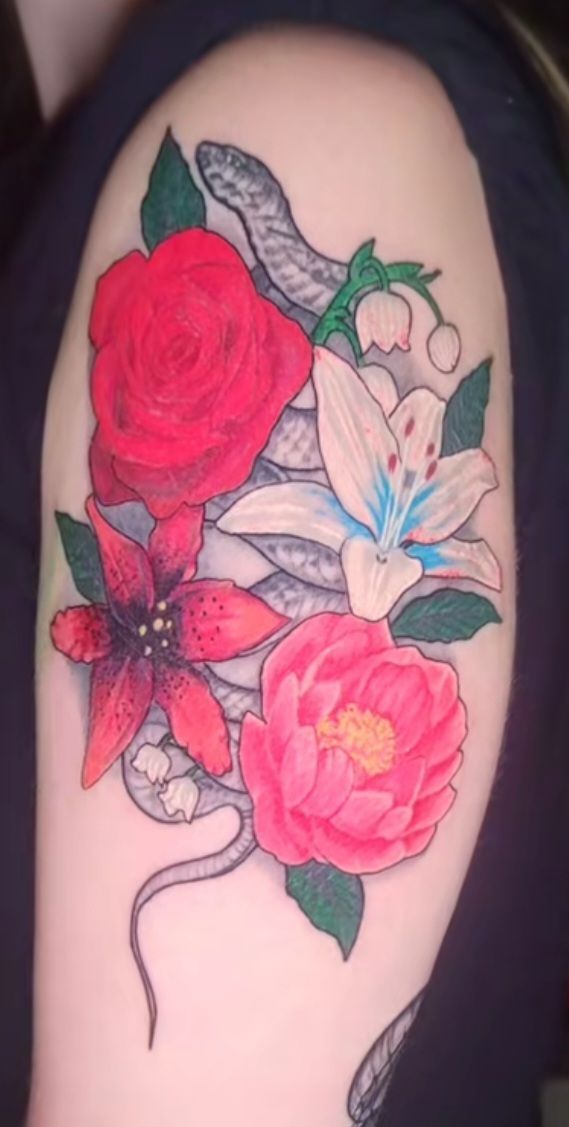 Tattoo of a grey snake winding through red, pink, and white flowers with green leaves on a person's arm.