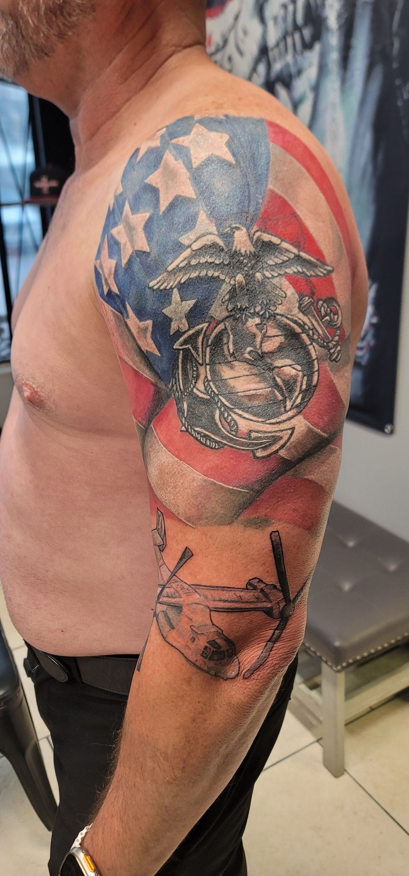 A man has a tattoo of an american flag and a marine on his arm.