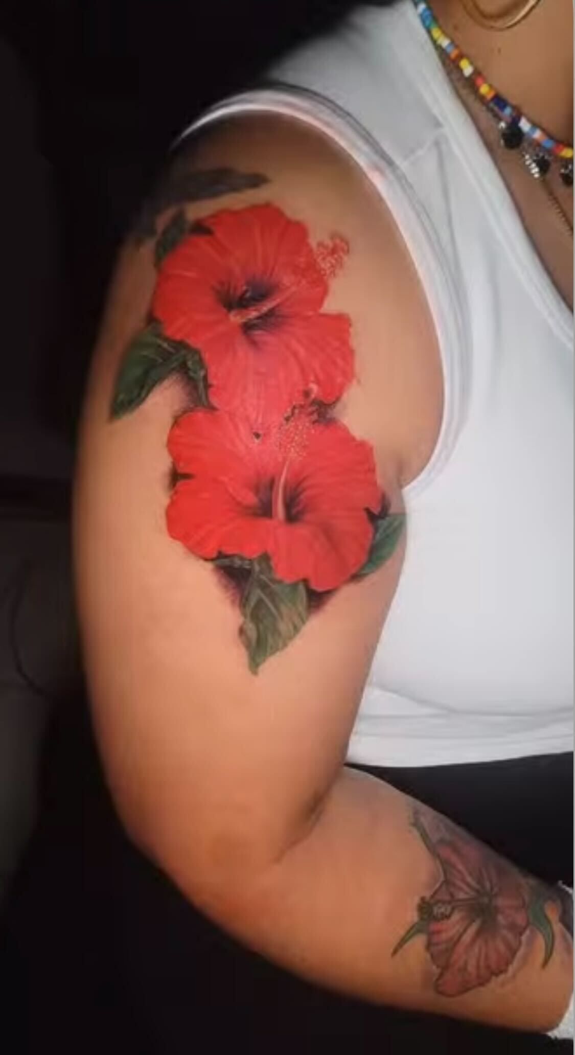 A woman has a tattoo of red hibiscus flowers on her shoulder.