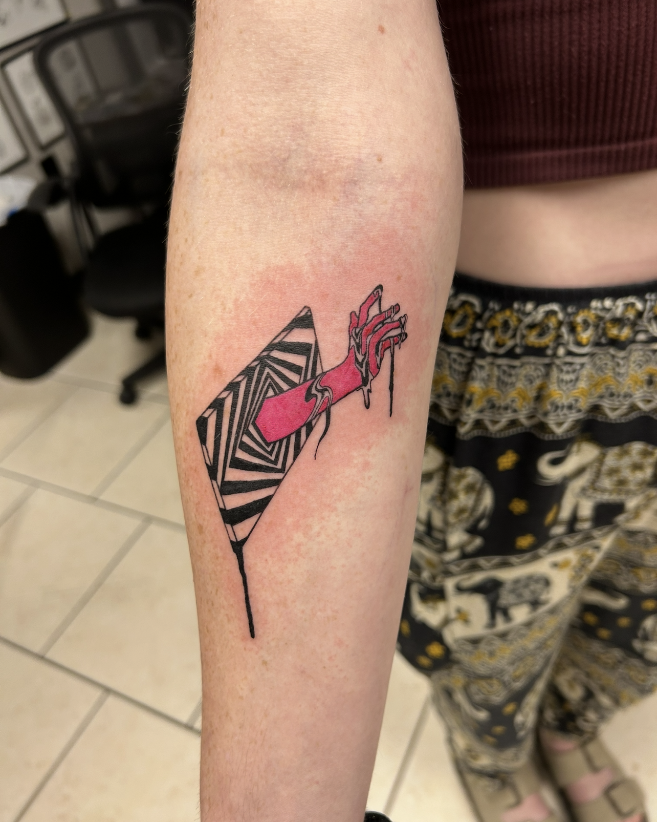 A colorful tattoo on an arm, featuring a zebra-striped design with pink nail polish dripping down.