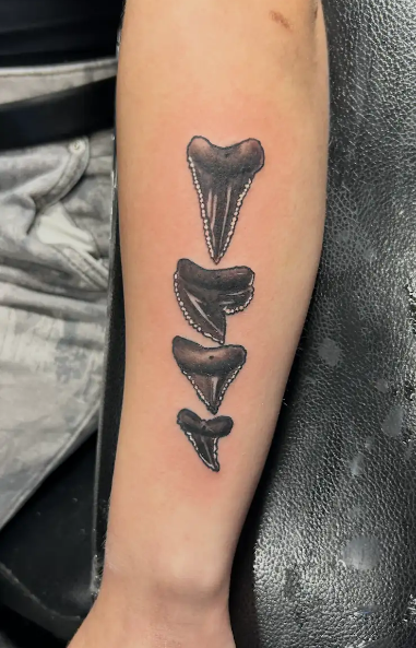 Tattoo of four jagged shark teeth lined vertically in black ink on a forearm.
