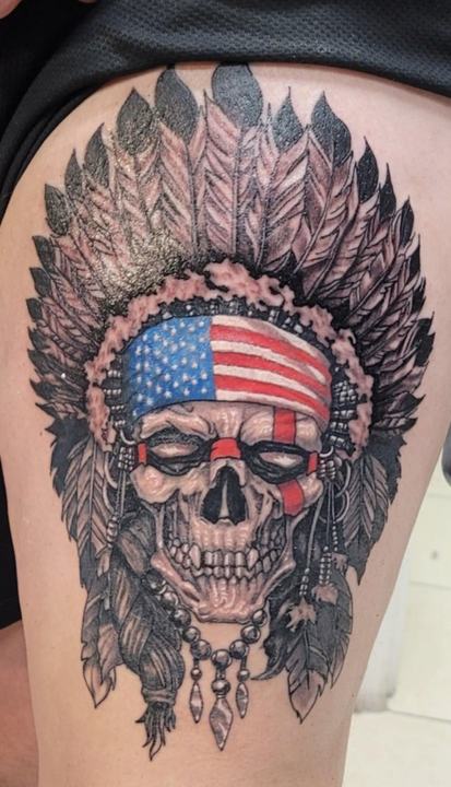 A person has a tattoo of a skull wearing a native american headdress.