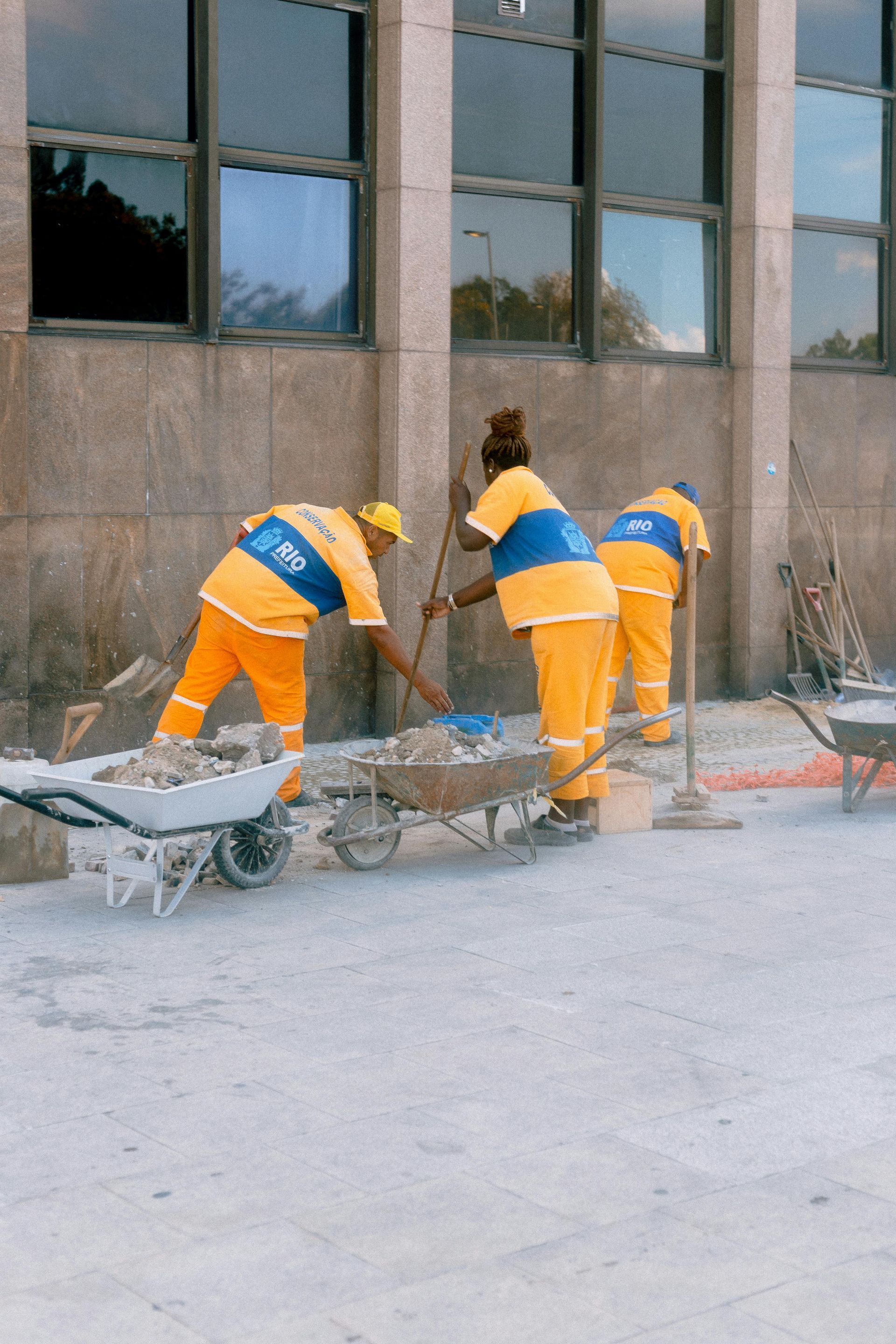 Tres trabajadores de saneamiento con uniformes naranjas limpiando el exterior de un edificio.