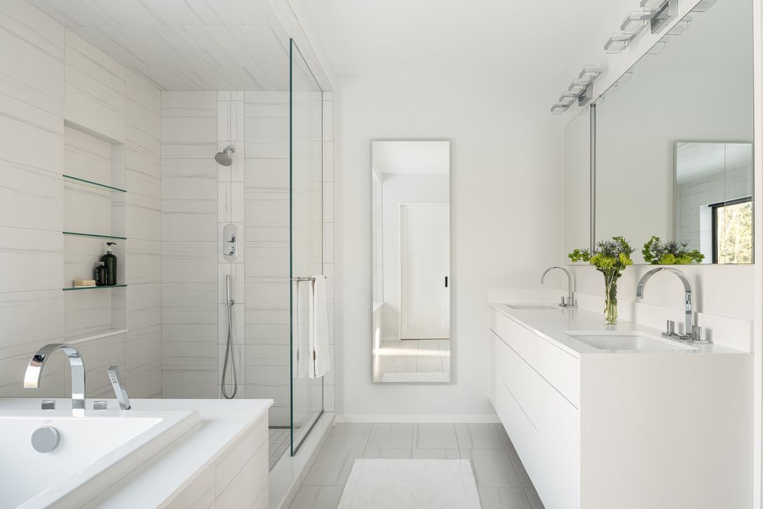 Bright modern white bathroom with bathtub, glass shower, vanity, and vase of flowers
