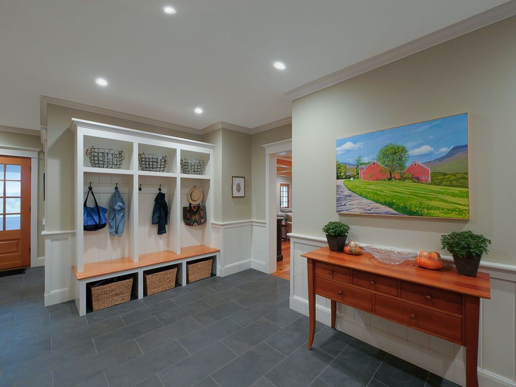 Bright entryway with coat hooks, benches, and a wooden console table beneath a landscape painting