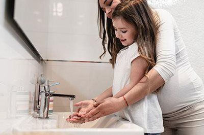 Woman helping child wash hands at a sink with running water.