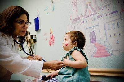 Doctor using a stethoscope on a child in a doctor's office with a princess castle mural.