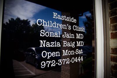 Window sign for Eastside Children's Clinic. Lists doctors Sonal Jain and Nazia Baig, phone number and open days.