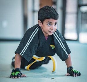 Boy in karate uniform doing push-ups on a gym floor, yellow belt visible.