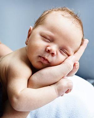 Sleeping newborn, resting on an open hand, light skin, short brown hair, neutral expression.