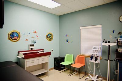 Pediatric exam room with blue walls, changing table, scale, and colorful chairs.