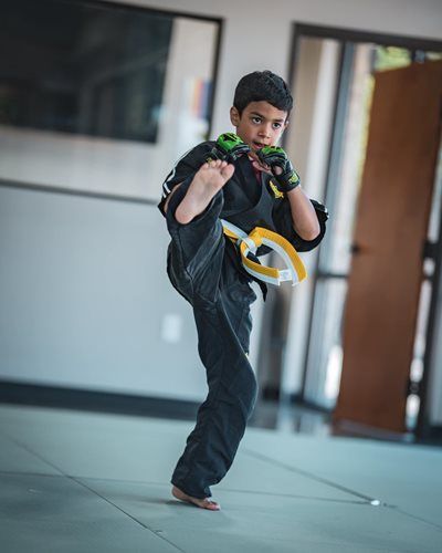 Young person in martial arts uniform kicking in a training space.