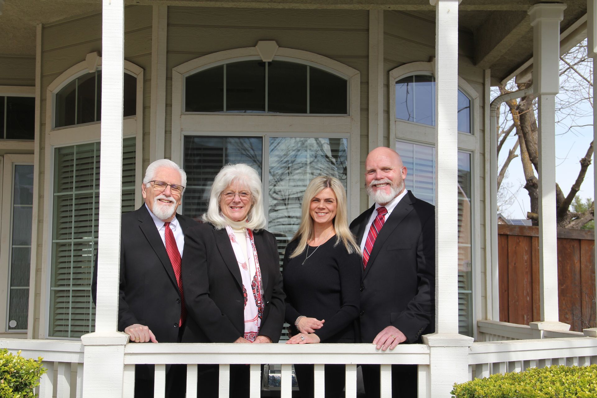 Four people in formal attire standing on a porch, smiling at the camera.