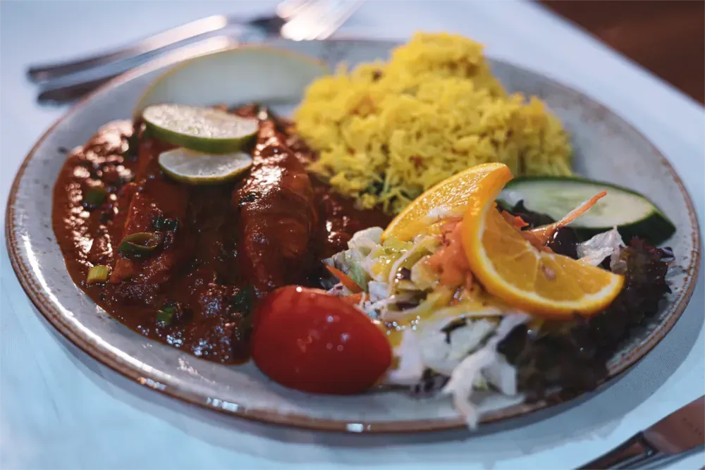 Tellergericht: Hühnercurry mit Reis, Salat, Tomate, Orangenscheibe und Limette.