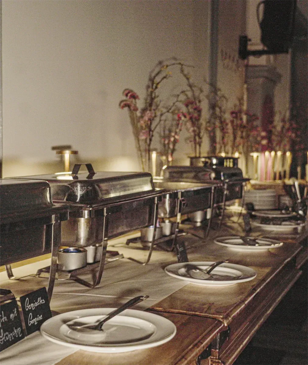 Buffettisch mit Edelstahl-Warmhaltebehältern und Tellern, gedeckt für eine Mahlzeit.
