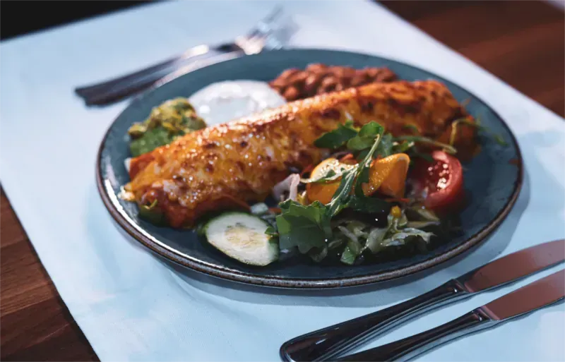 Ein Teller mit einem großen Burrito, Salat, Bohnen, Guacamole und Sauerrahm.