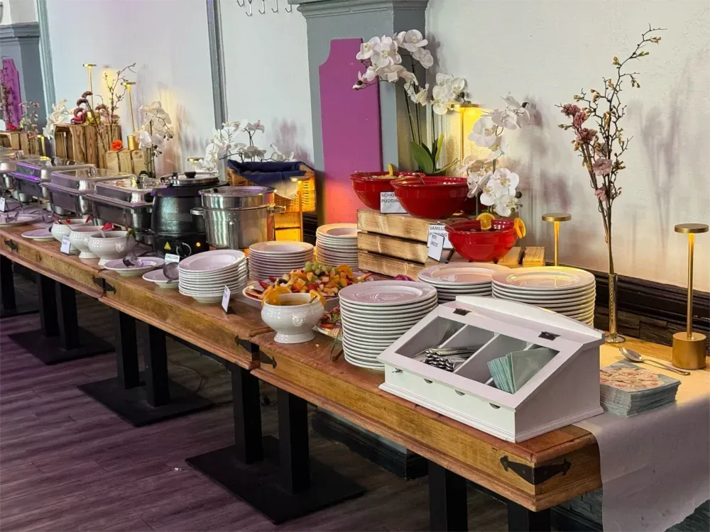 Buffet mit verschiedenen Speisen und Servierutensilien, dekoriert mit Blumen.