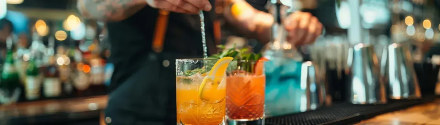 Ein Barkeeper rührt in einer Bar einen Cocktail mit Orangenscheibe um.