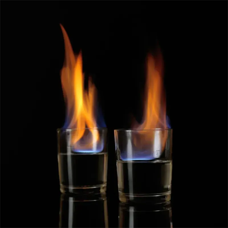 Zwei Schnapsgläser mit Sambuca über denen jeweils eine blau-orange Flamme über der Flüssigkeit brennt. Schwarzer Hintergrund.
