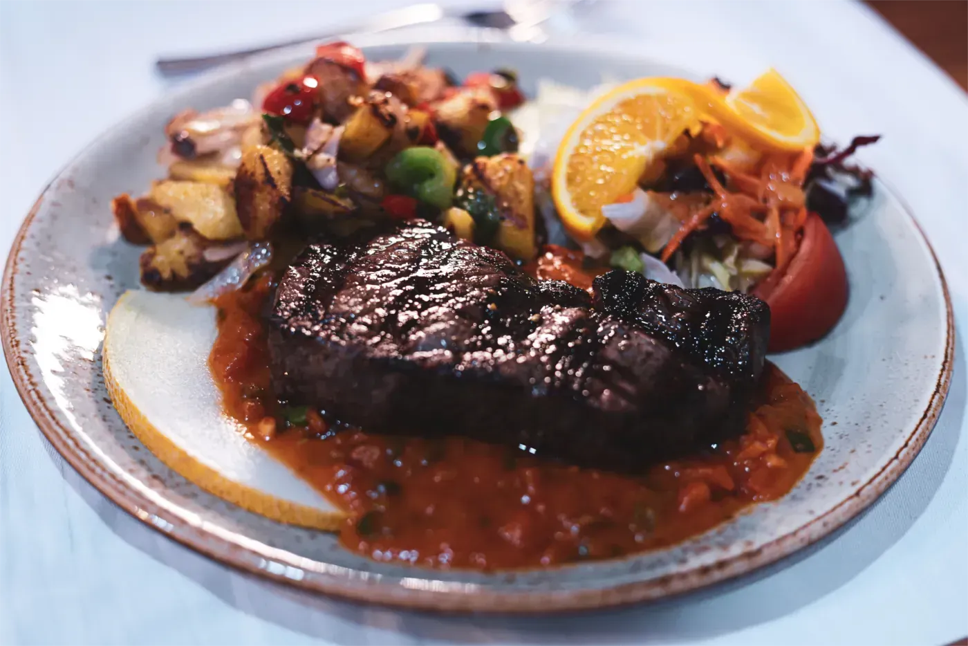Steak mit Sauce, geröstetem Gemüse, Obst und Salat auf einem Teller.
