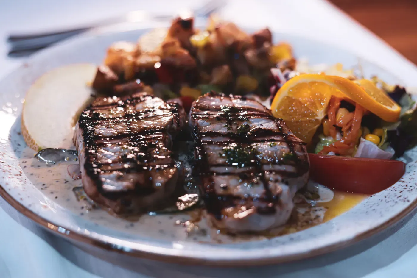 Gegrilltes Steak mit Kartoffeln, Salat und Orangenscheiben auf einem weißen Teller.