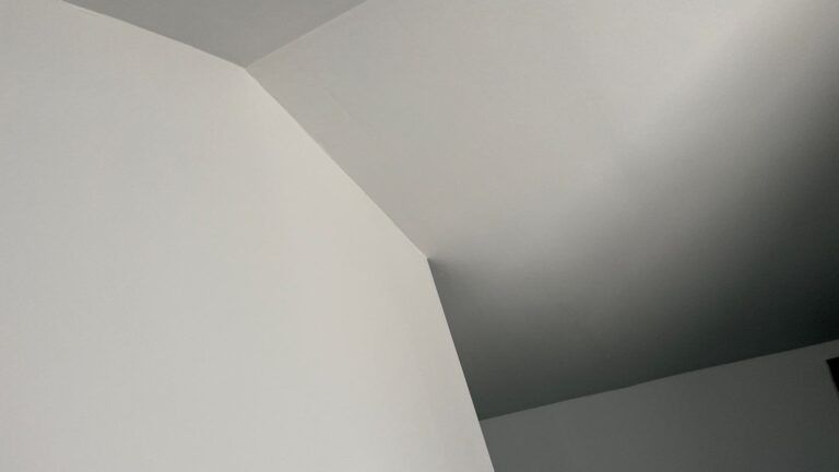 A corner of a room with a white wall and a black ceiling.