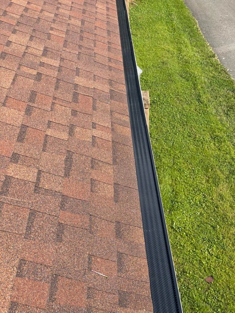 A close up of a gutter on a roof next to a grassy area.