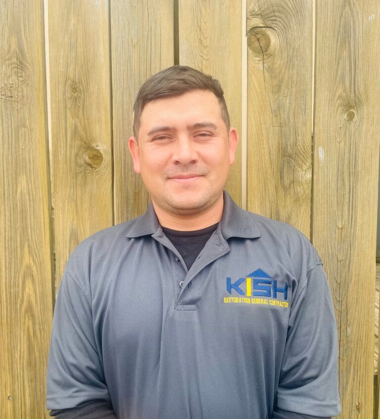A man wearing a kash shirt is standing in front of a wooden fence.
