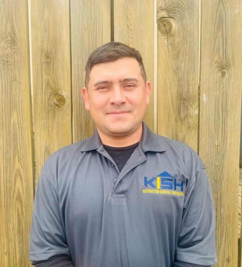A man wearing a kash shirt is standing in front of a wooden fence.