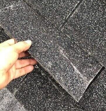A person is holding a piece of shingles in their hand.
