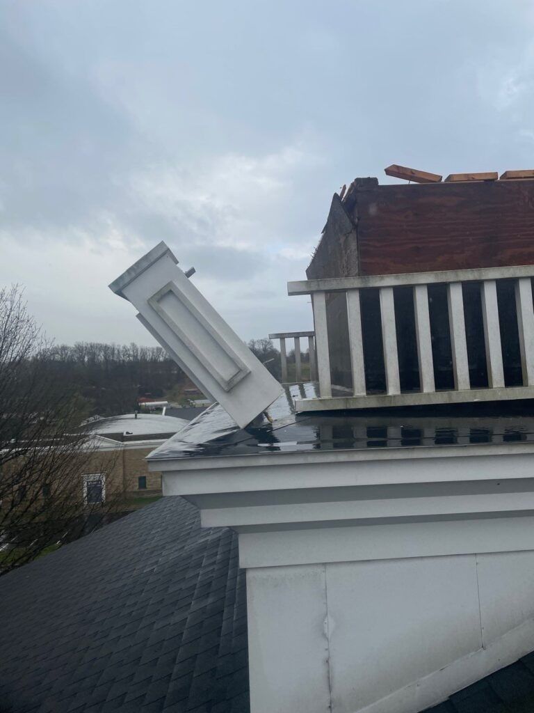 A white building with a roof that has been damaged by a storm.