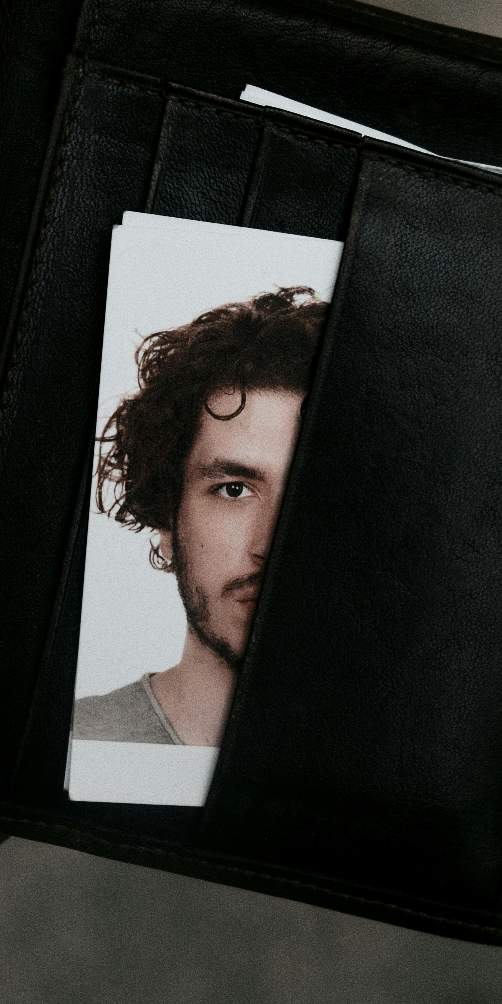 A man with curly hair is peeking out of a black wallet.