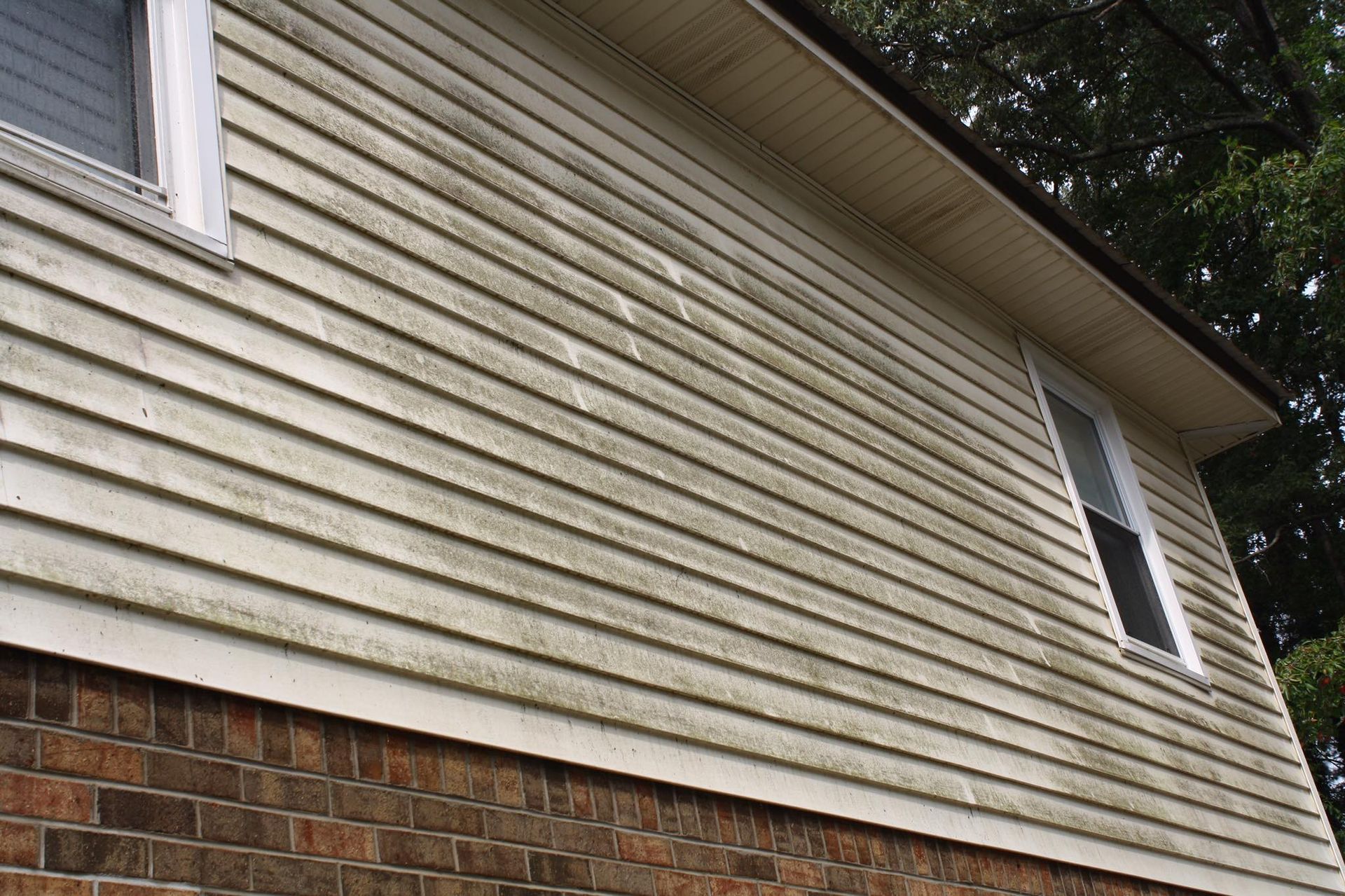 A house with a dirty siding and a brick wall.