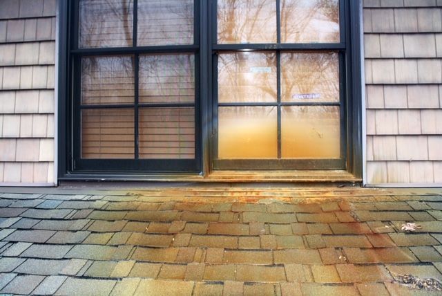 A window on the side of a house with a brick patio in front of it.