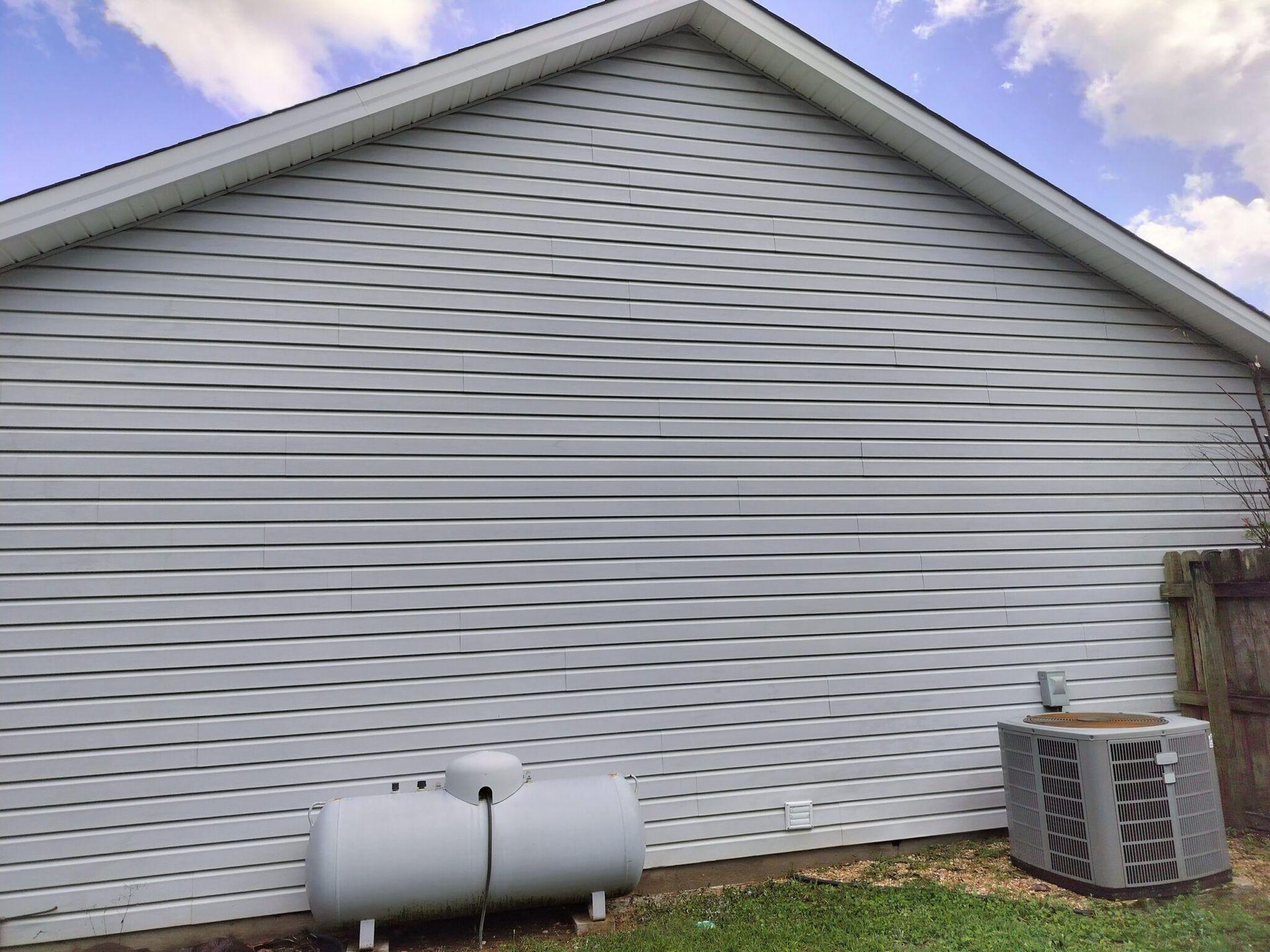 A white house with a propane tank and air conditioner on the side.