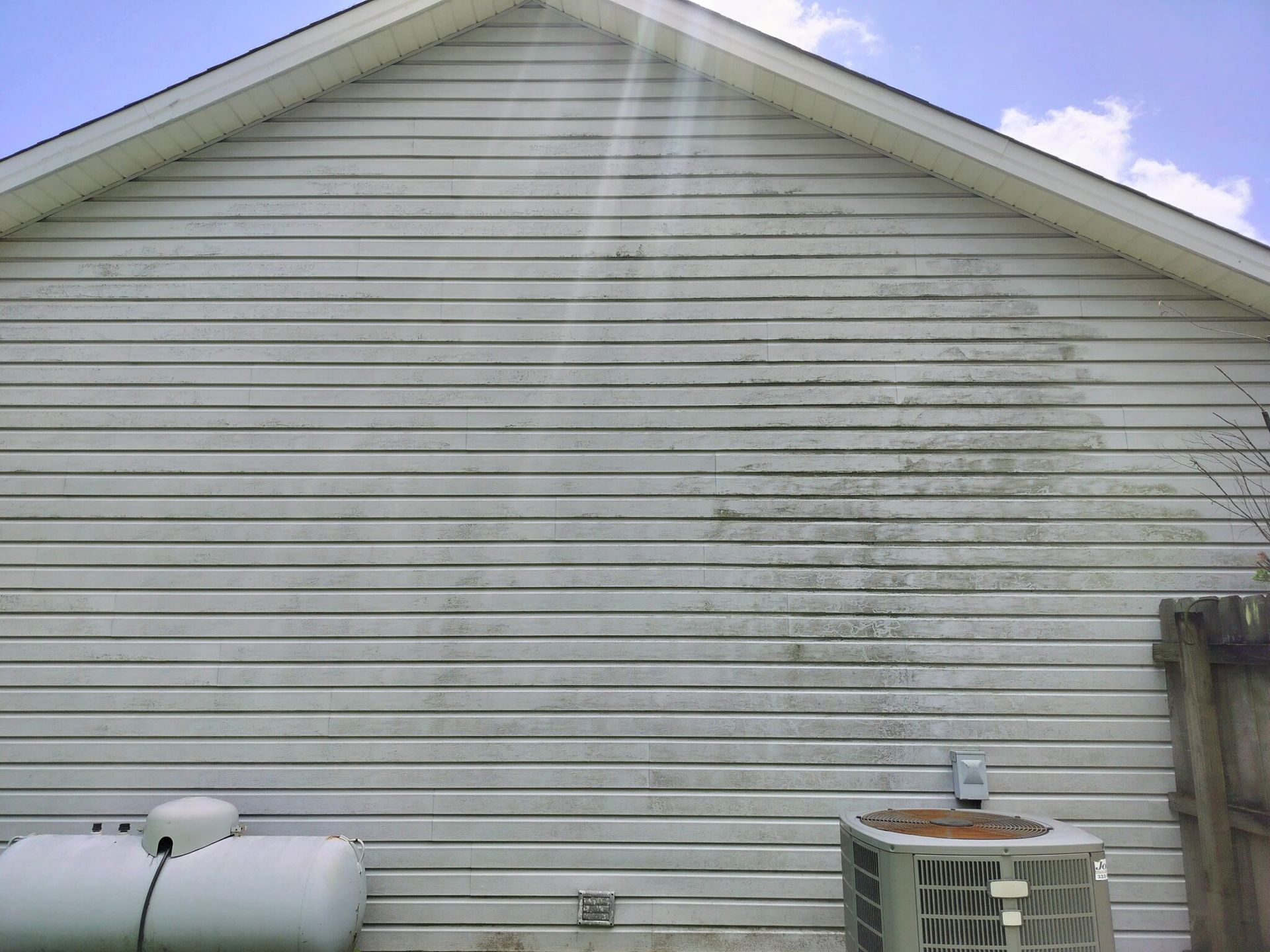 A white house with a dirty siding and an air conditioner.