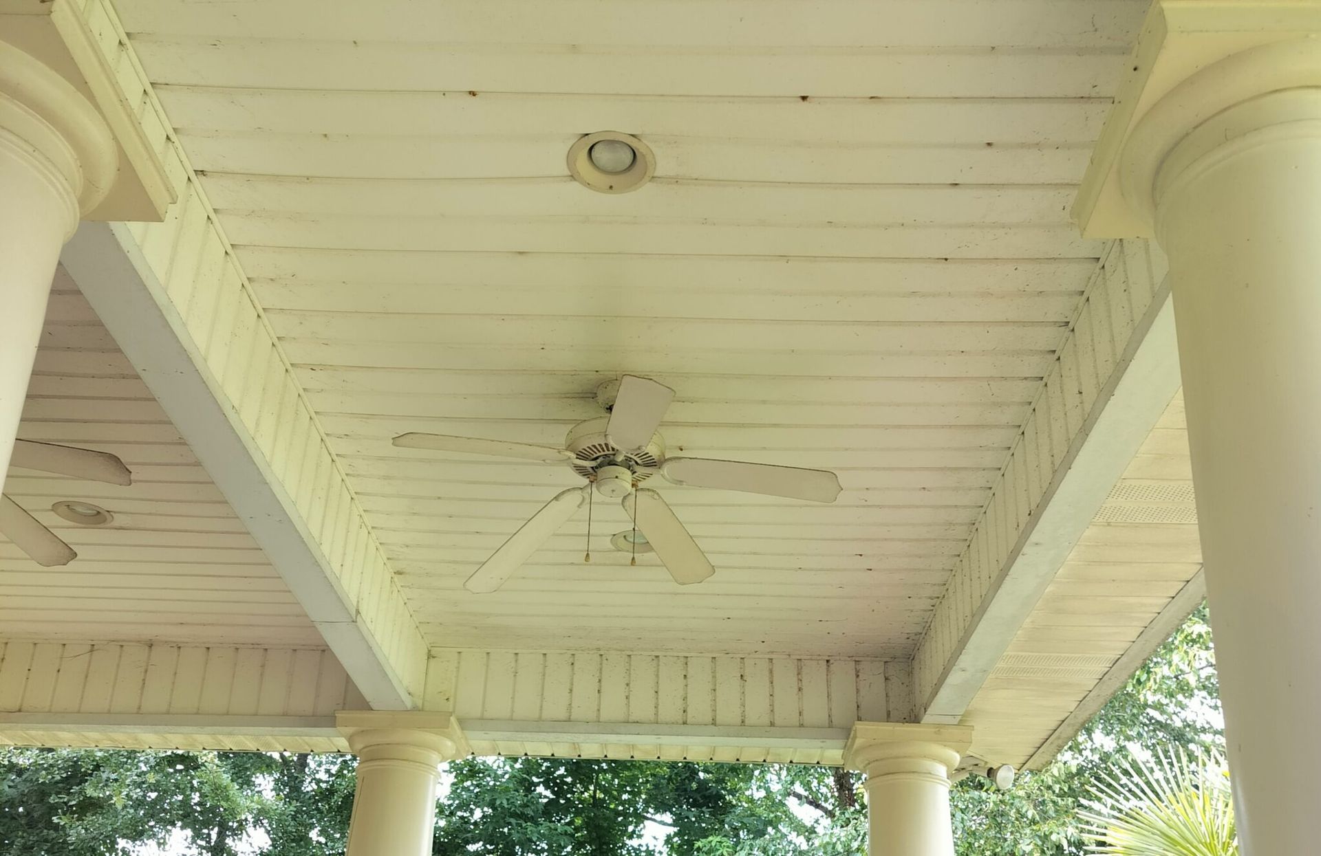 A ceiling fan is hanging from the ceiling of a porch.