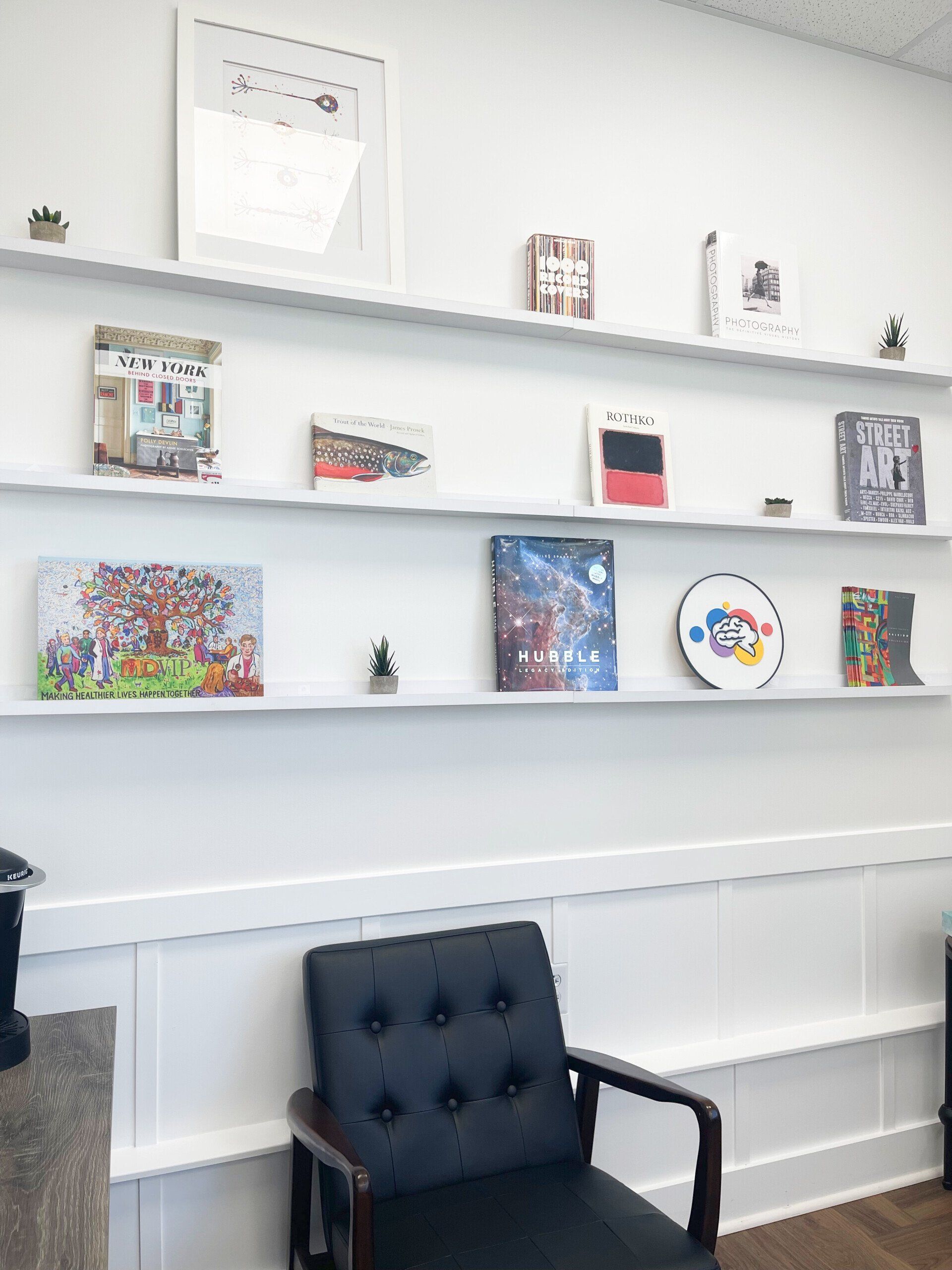 A waiting room with a chair , shelves , and paintings on the wall.