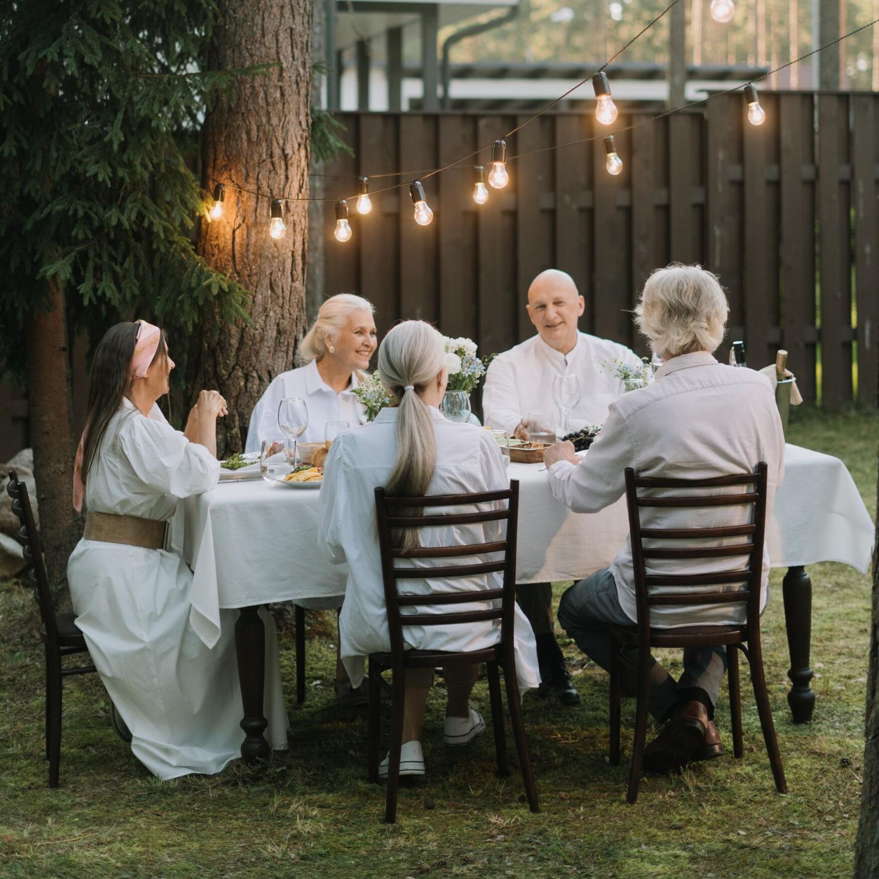 A group of people are sitting around a table in a backyard.