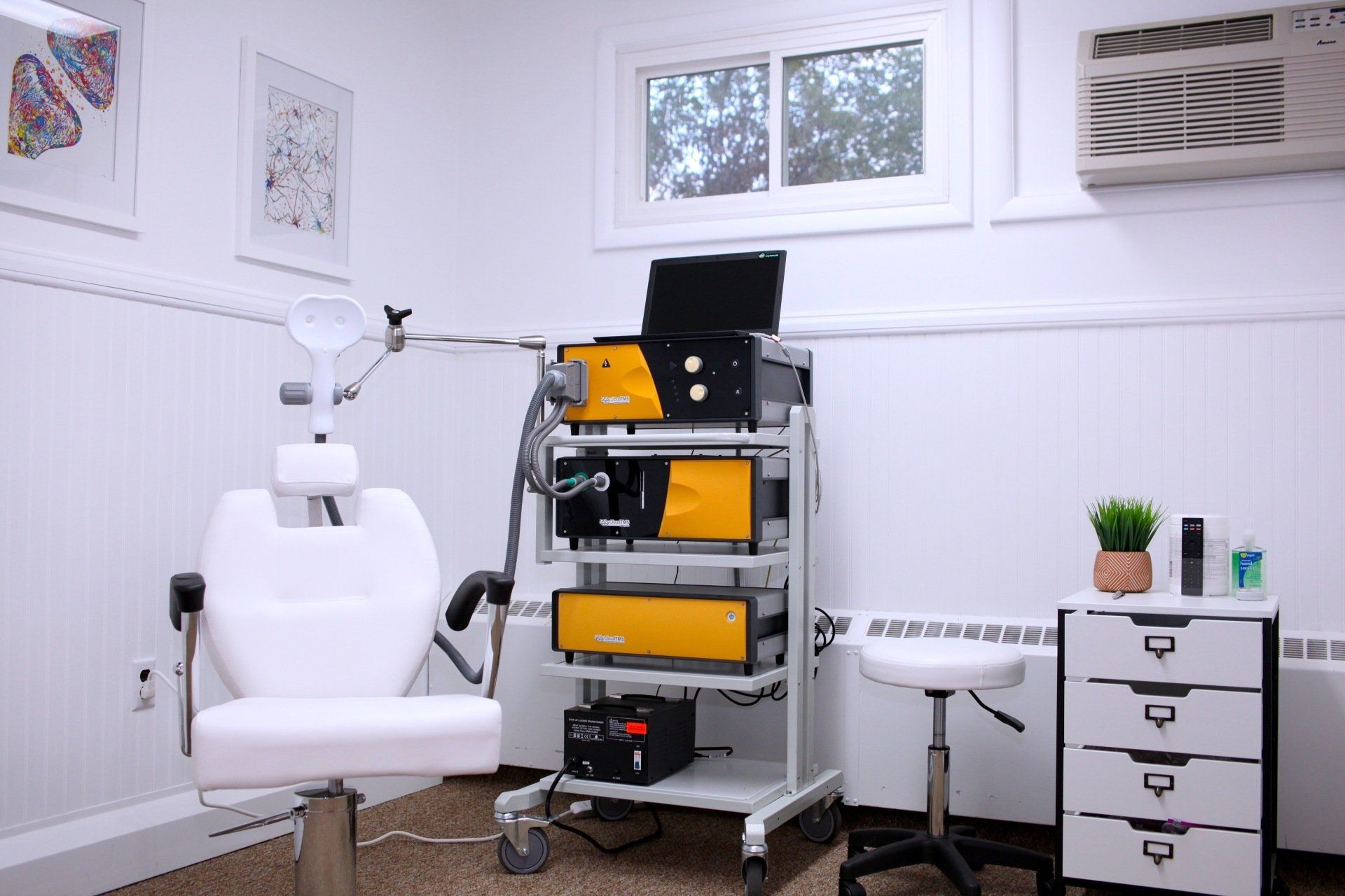 A doctor 's office with a chair and a cart with a laptop on it.