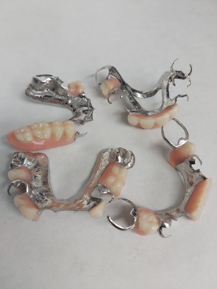 A Bunch of Dentures Are Laying on a White Surface — Complete Denture Clinic in Kanwal, NSW