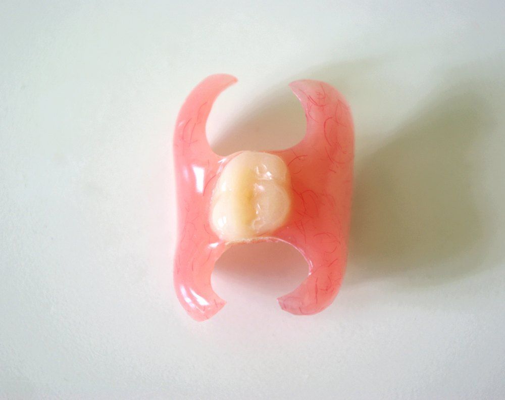 A Pink Denture With a Tooth in It is Sitting on a White Surface — Complete Denture Clinic in Kanwal, NSW