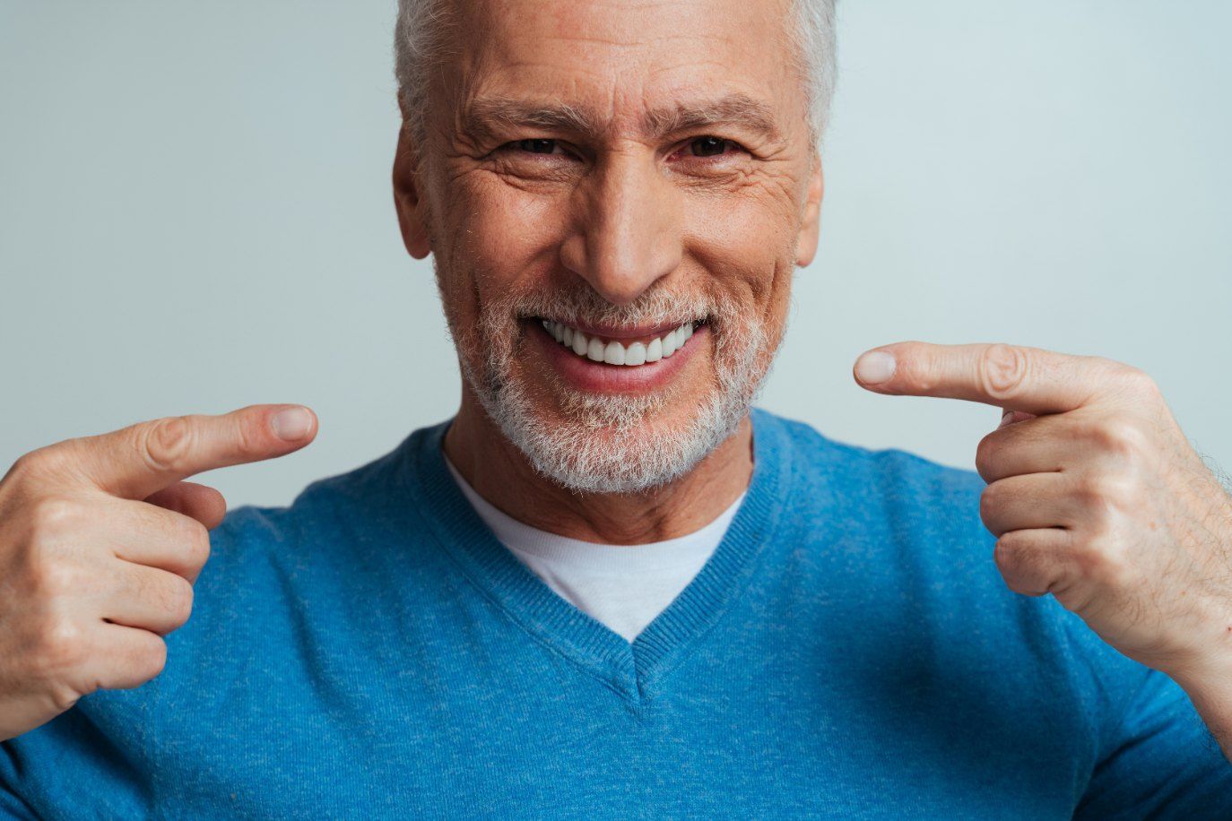 An Older Man is Pointing at His Teeth and Smiling — Complete Denture Clinic in Budgewoi, NSW