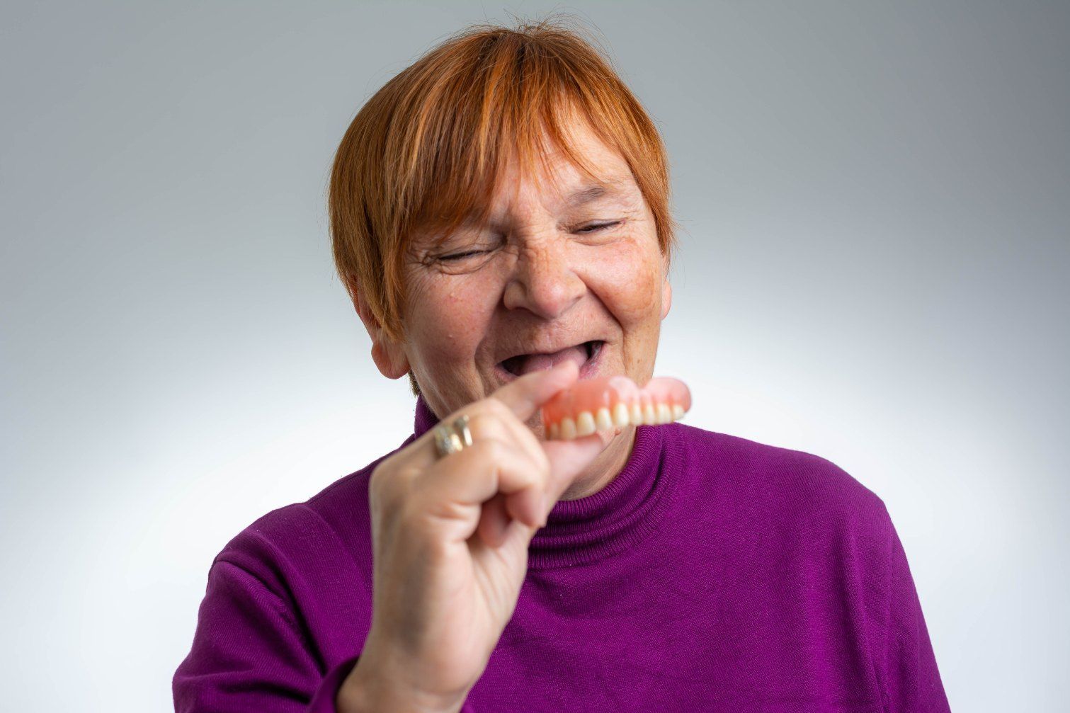 An Elderly Woman is Holding a Denture in Her Mouth — Complete Denture Clinic in Wyong, NSW