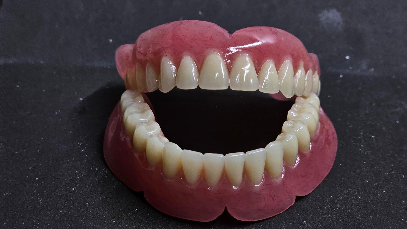 A Close Up of a Denture With Its Mouth Open on a Black Surface — Complete Denture Clinic in Wyong, NSW