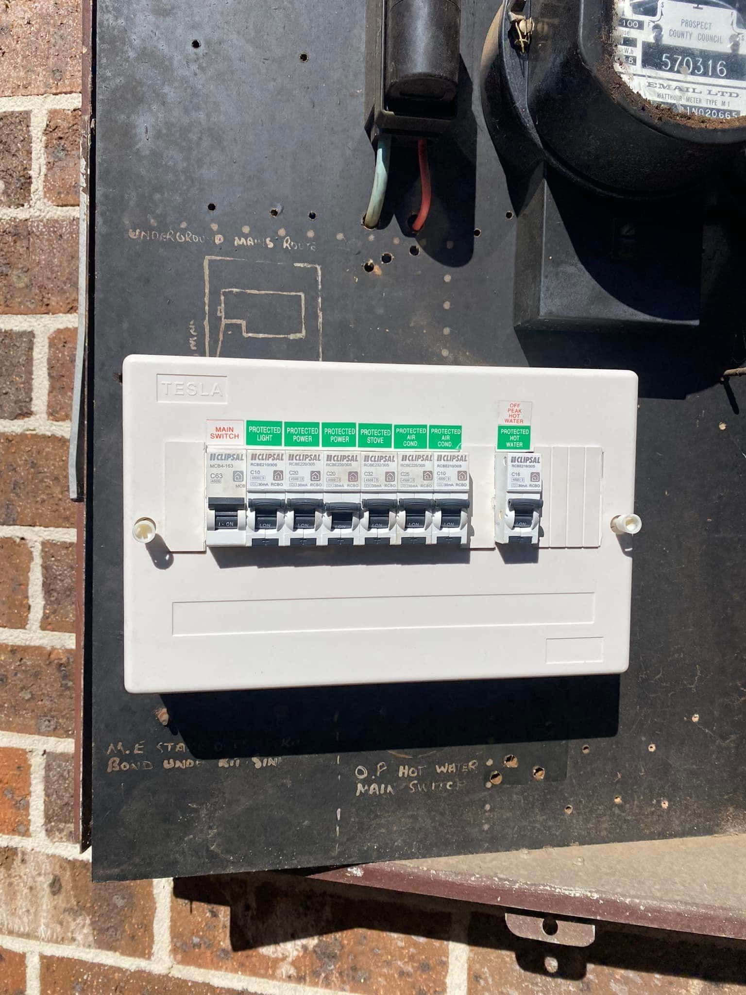 A White Electrical Fuse Box Mounted on a Brick Wall — SparkSafe Electrical in Dapto, NSW