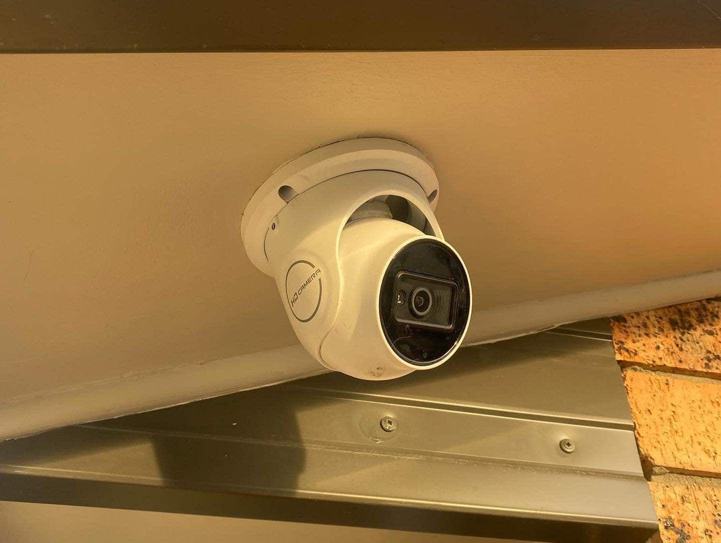 White Security Camera Mounted on a Beige Ceiling, Pointing Downwards — SparkSafe Electrical in Dapto, NSW