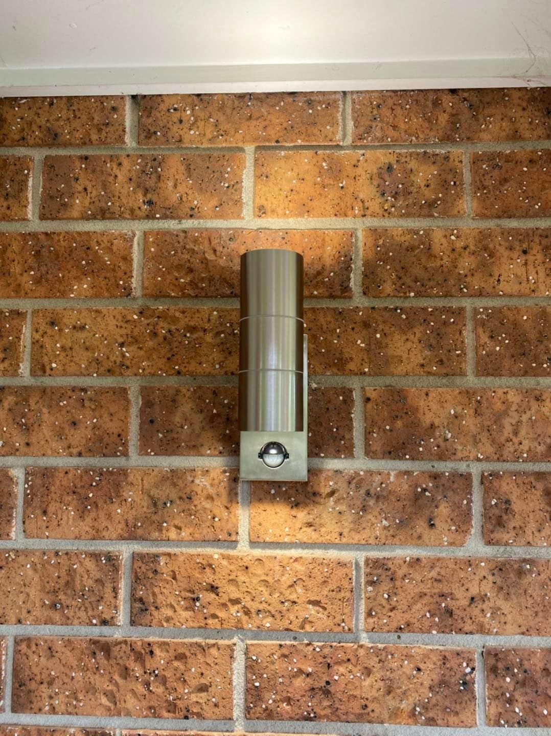 Stainless Steel Outdoor Wall Light Fixture on a Red-brown Brick Wall — SparkSafe Electrical in Dapto, NSW