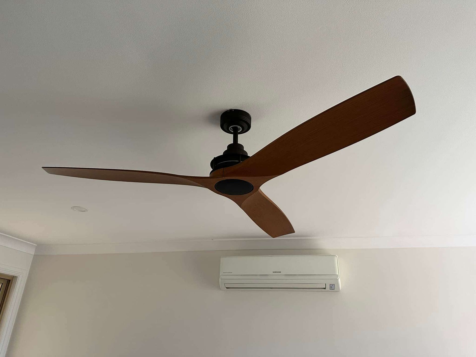 Ceiling Fan With Three Wooden Blades, Black Motor, Mounted on a White Ceiling — SparkSafe Electrical in Bulli, NSW
