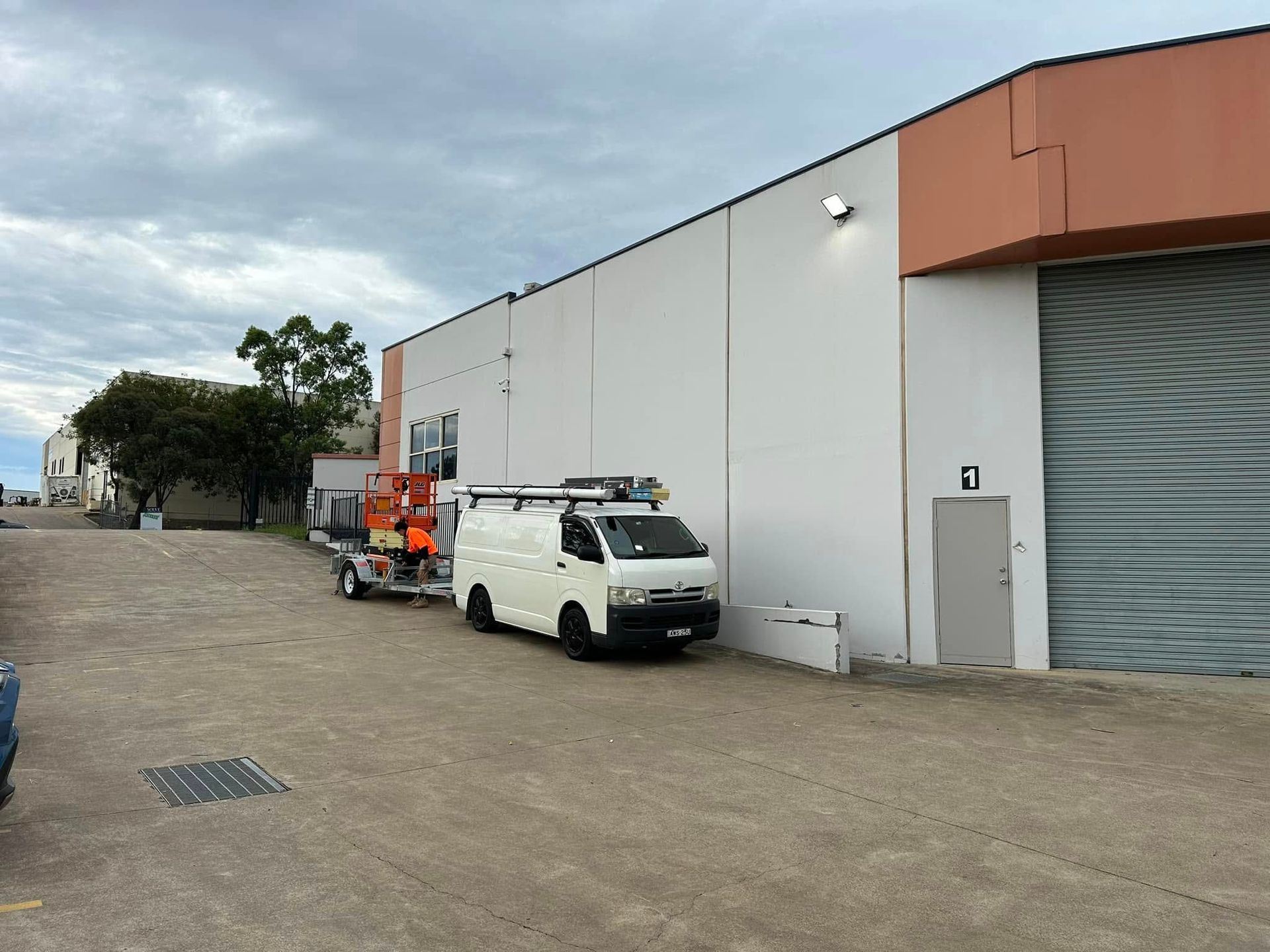 White van towing machinery trailer parked near a warehouse, overcast sky — SparkSafe Electrical in Gerringong, NSW